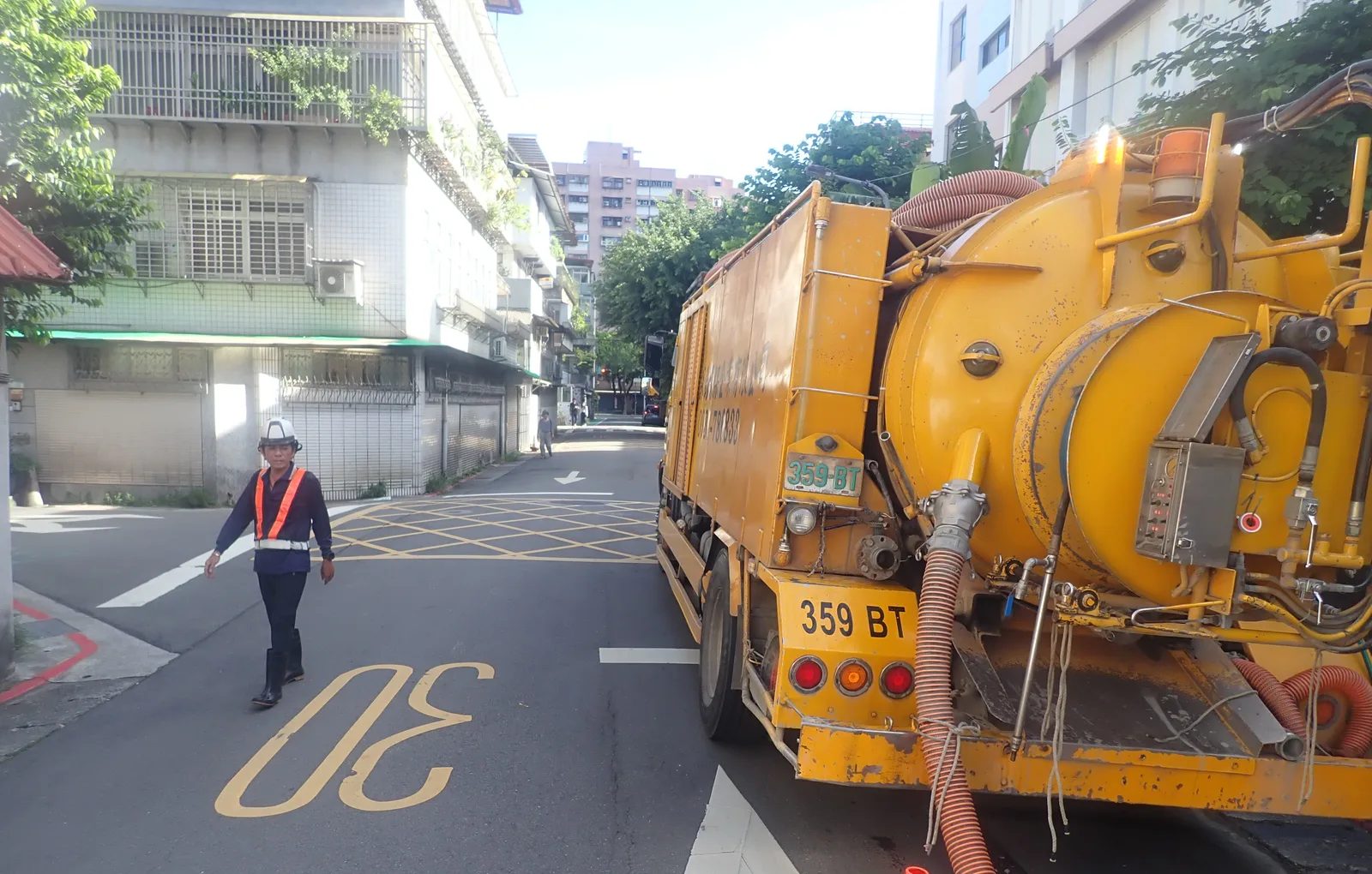 黃色清溝車停在路邊，吸管拉向地面，穿反光背心的人員在路口指揮