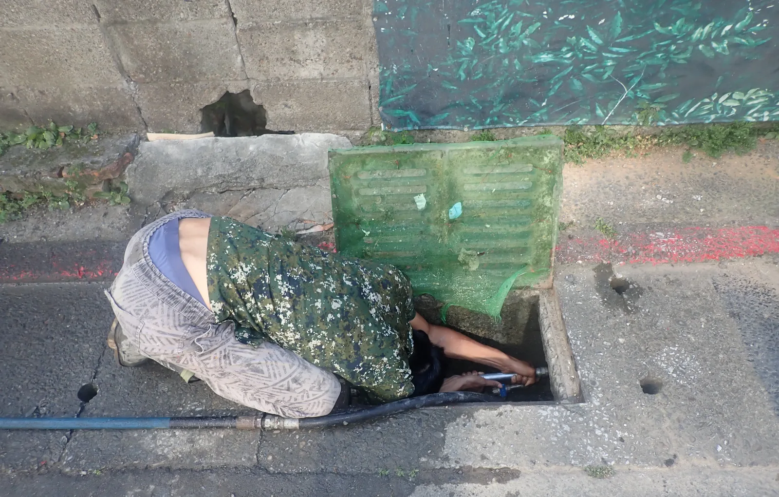 穿迷彩衣的師傅趴在掀開蓋板的溝口，把手伸進溝裡