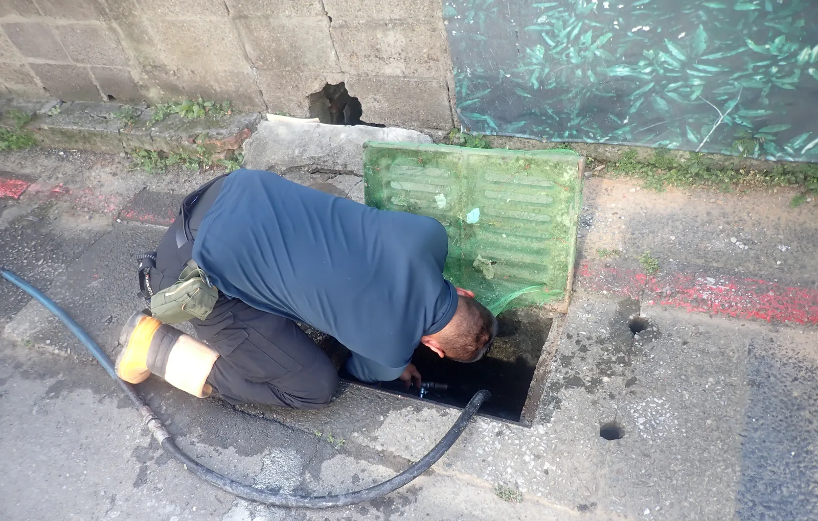 穿深藍上衣的師傅跪在路邊，把頭和手探進溝口