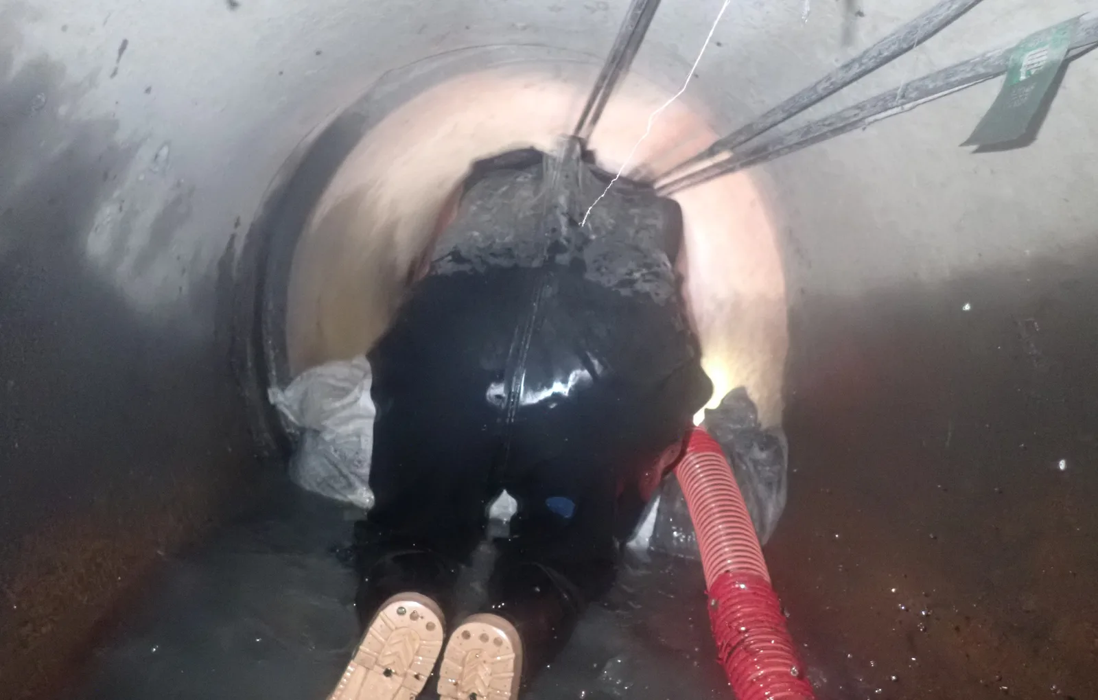 師傅跪在圓形管道裡往前作業，旁邊是紅色吸管與裝泥的袋子