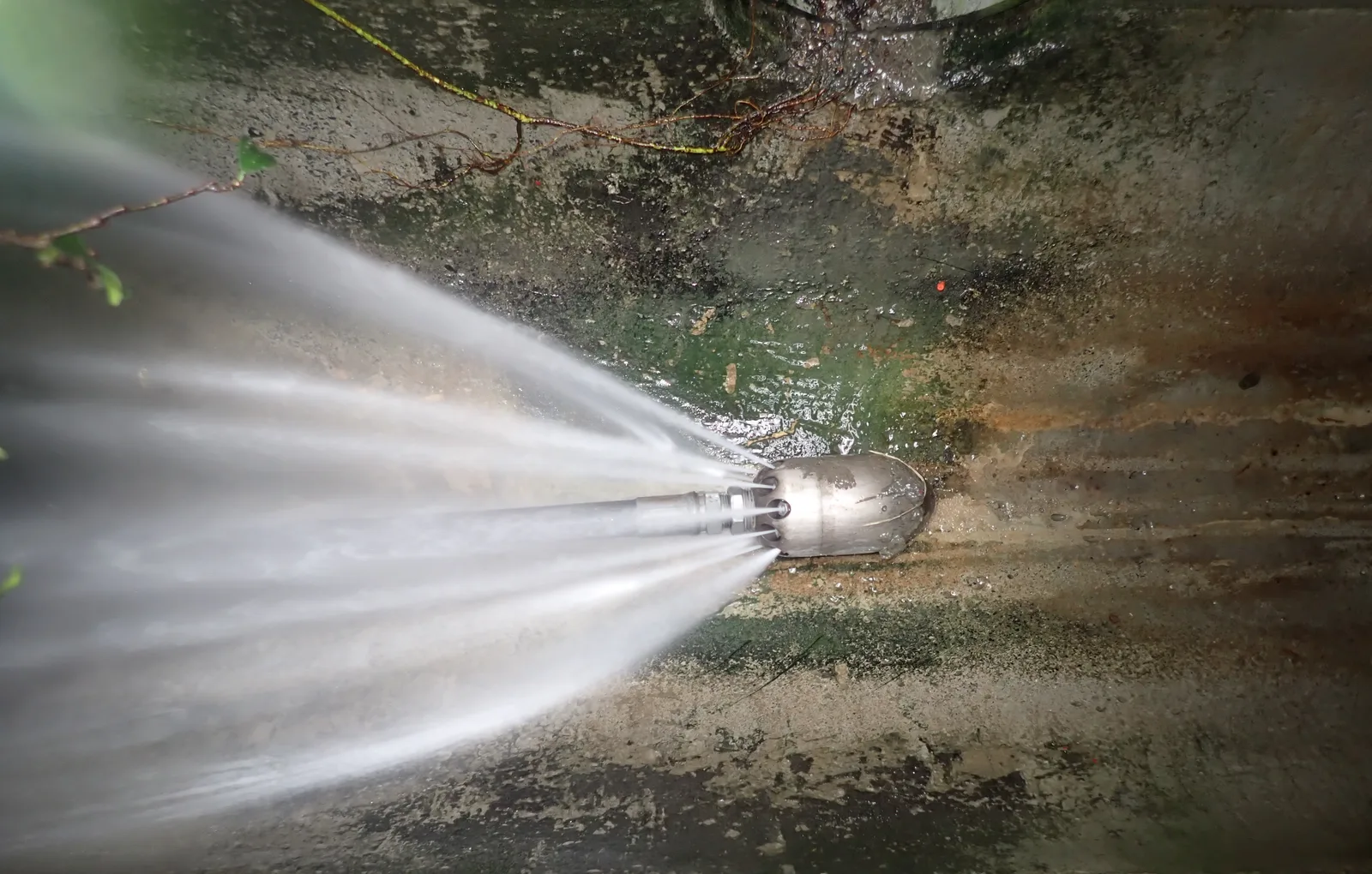 高壓噴頭在箱涵內向後噴出多道水柱，沖刷溝底