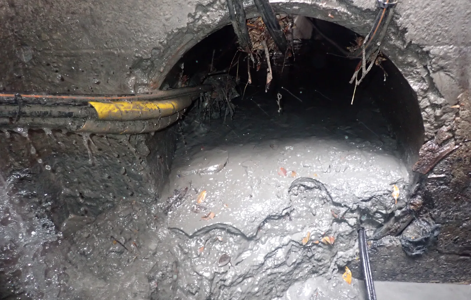 涵管管口堆滿灰色淤泥，上方穿過一束電纜