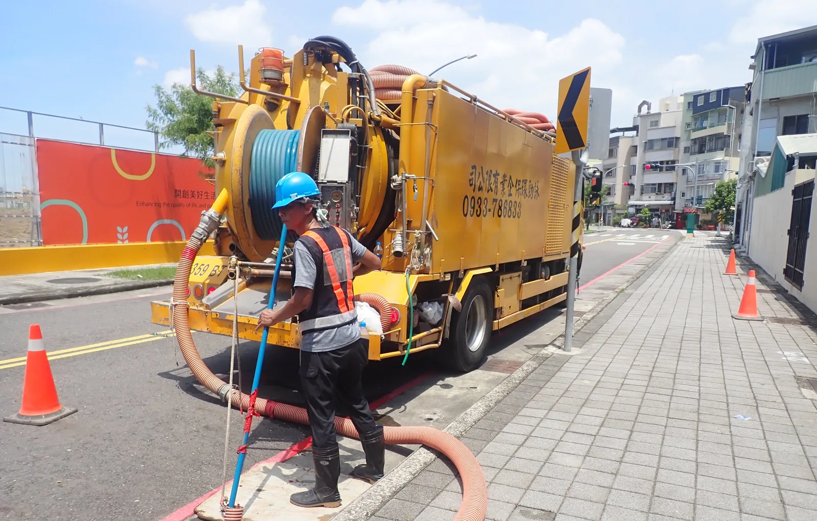 黃色清溝車停在路邊,戴藍色安全帽的師傅拉著抽吸管作業
