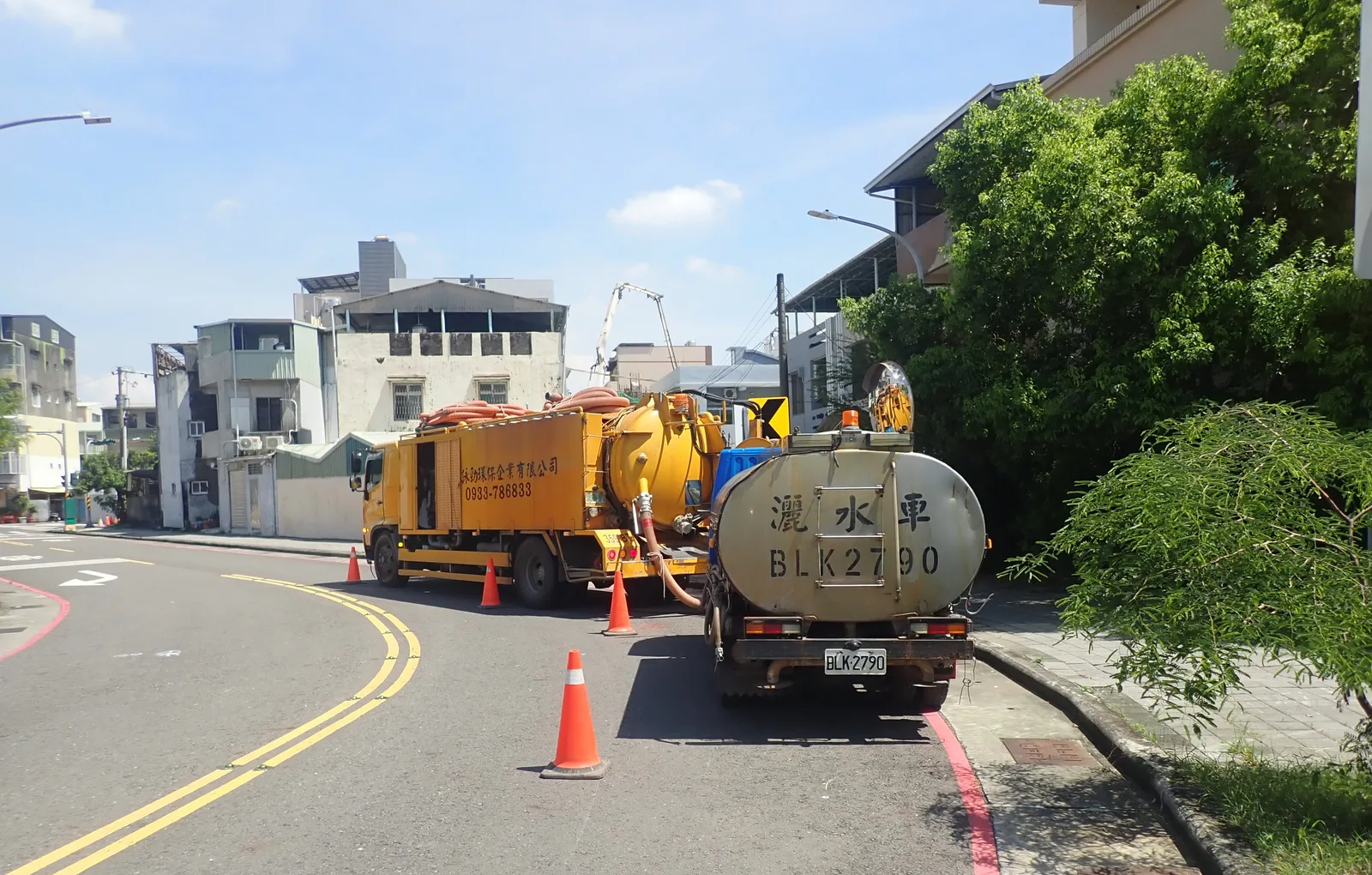 黃色清溝車與白色水車停在彎道路邊,前後擺著三角錐