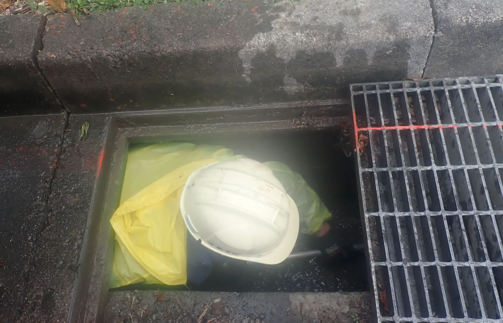 側溝疏通施工中:格柵旁打開的溝口,裡面放著白色安全帽與黃色袋子